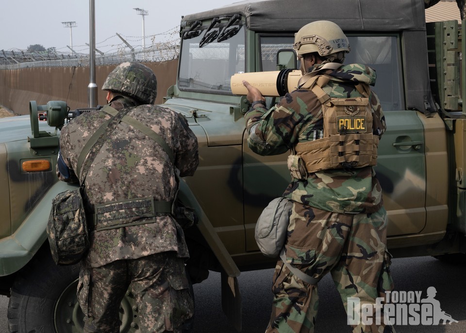 한국공군 38전투비행전단 군사경찰(왼쪽)이 K2C1 소총을 겨누고 있는 가운데 미 공군 1중대가 조준 사격을 하고 있다. 2023년 2월 7일, 계획과 프로그램을 담당하는 제8 보안군 중대장 브라이언트 애쉬가 한국 군산 공군 기지의 소형 무인기 저지 훈련에서 드론버스터를 조준하고 있다. 드론버스터는 적의 드론을 무력화할 수 있는 무선 주파수 교란기다.(사진:U.S.Air Force)